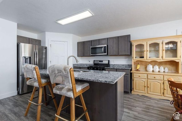 1142 W Honeycomb Dr, Grantsville, UT 84029 - kitchen featuring appliances with stainless steel finishes, a kitchen bar, glass insert cabinets, dark wood-type flooring, and a center island with sink