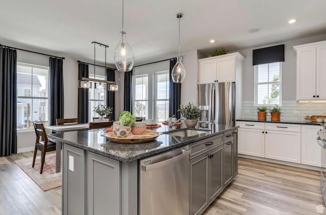 1028 N 1420 W Unit 31, Pleasant Grove, UT 84062 - kitchen featuring appliances with stainless steel finishes, a sink, an island with sink, light wood-style floors, and dark stone counters