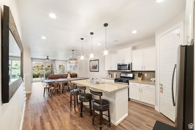 5048 N Escapes Dr, St George, UT 84770 - kitchen featuring appliances with stainless steel finishes, wood finished floors, backsplash, white cabinetry, and light stone countertops