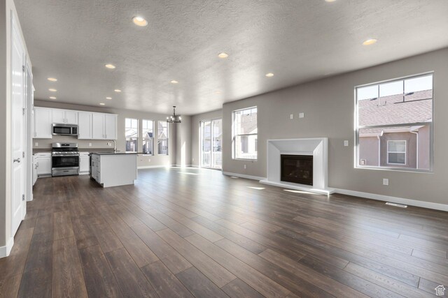 6564 N Bald Unit D195, Eagle Mountain, UT 84005 - unfurnished living room with a sink, recessed lighting, a chandelier, a glass covered fireplace, and dark wood finished floors
