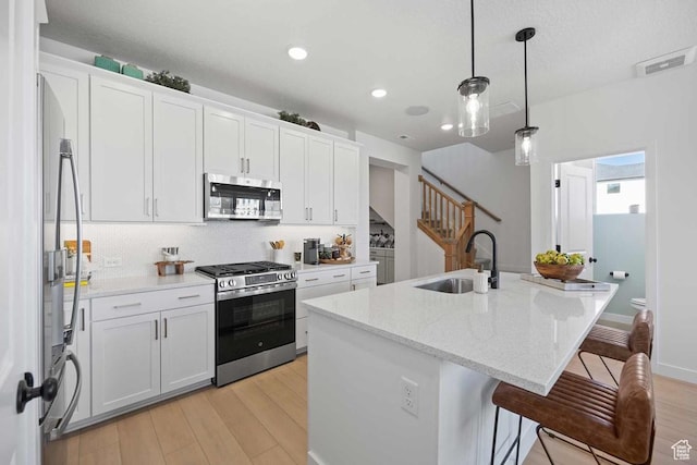 2854 S Ritter Row Unit 52, West Valley City, UT 84128 - kitchen with appliances with stainless steel finishes, a sink, light wood-style floors, tasteful backsplash, and an island with sink