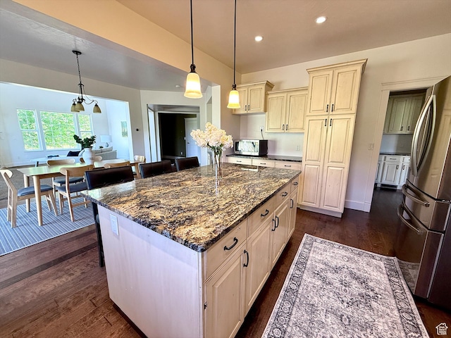 2307 Maple Leaf Dr, Cove, UT 84320 - kitchen with appliances with stainless steel finishes, cream cabinetry, dark wood-type flooring, a breakfast bar area, and dark stone countertops