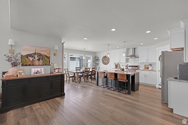 12473 S Desert Mesa Dr, Herriman, UT 84096 - kitchen with stainless steel appliances, wall chimney range hood, a kitchen island with sink, light wood-style floors, and decorative backsplash
