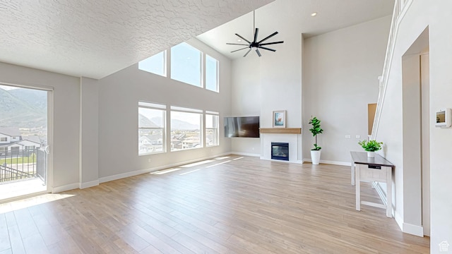 833 N Union Bench Dr W Unit 62, Mapleton, UT 84664 - unfurnished living room with a glass covered fireplace, light wood-style flooring, baseboards, a textured ceiling, and a ceiling fan