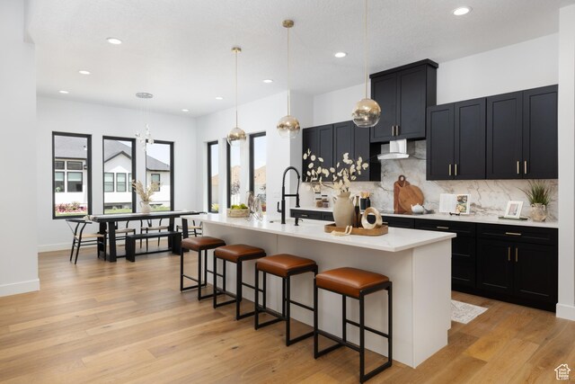 6552 W Timber Ranch Dr, Herriman, UT 84096 - kitchen with wall chimney range hood, light countertops, backsplash, a breakfast bar area, and recessed lighting