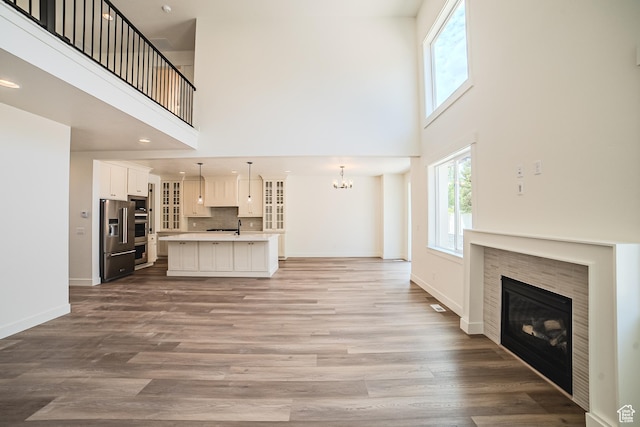 10926 S Little Sahara Dr Unit 1002, South Jordan, UT 84009 - unfurnished living room featuring a towering ceiling, a tiled fireplace, a chandelier, wood finished floors, and baseboards