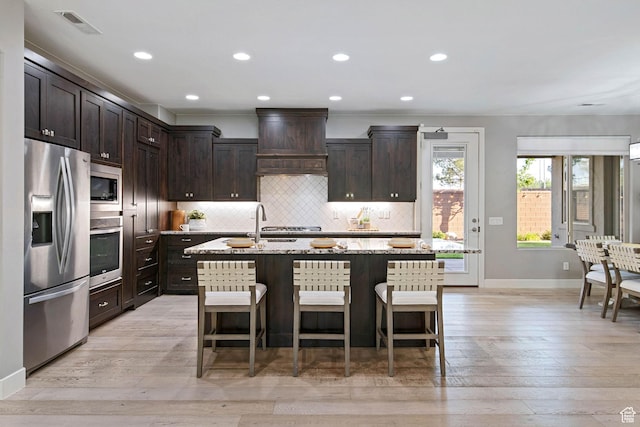 2914 E 1880 S, St George, UT 84790 - kitchen with appliances with stainless steel finishes, premium range hood, tasteful backsplash, dark brown cabinets, and light wood-type flooring