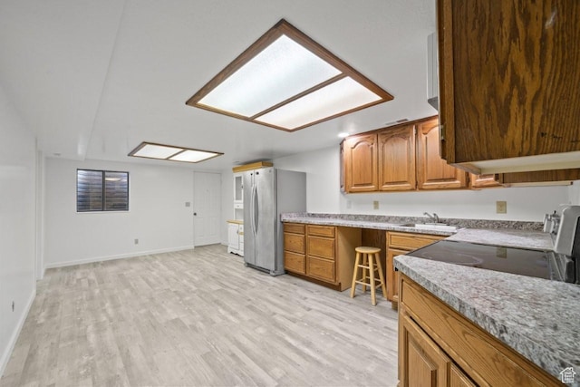 2045 W 5025 S, Roy, UT 84067 - kitchen featuring freestanding refrigerator, brown cabinets, light wood-style flooring, light countertops, and a skylight