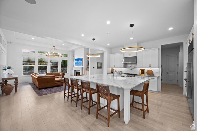 4771 W Juniper Bend Cir, Herriman, UT 84096 - kitchen with under cabinet range hood, a breakfast bar area, white cabinetry, tasteful backsplash, and light stone counters