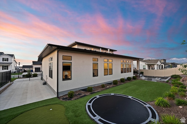 4771 W Juniper Bend Cir, Herriman, UT 84096 - rear view of house featuring a trampoline, a patio, an area to practice putting, and stucco siding