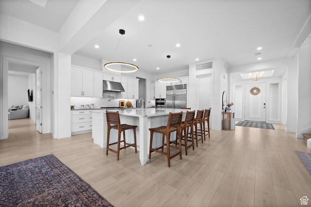 4771 W Juniper Bend Cir, Herriman, UT 84096 - kitchen featuring stainless steel appliances, under cabinet range hood, a kitchen bar, a spacious island, and white cabinetry