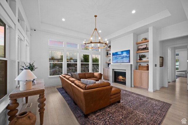4771 W Juniper Bend Cir, Herriman, UT 84096 - living area with a tray ceiling, a chandelier, light wood finished floors, a glass covered fireplace, and recessed lighting