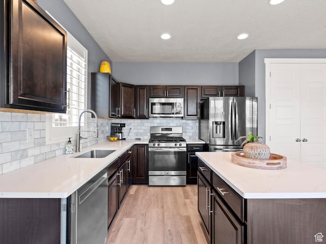 9558 S Lea Heather Way, West Jordan, UT 84081 - kitchen with appliances with stainless steel finishes, a sink, dark brown cabinetry, a center island, and light wood-style floors