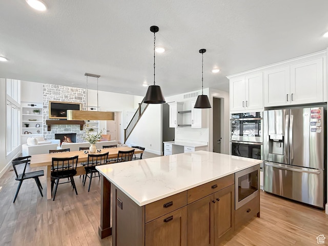 2558 N 1150 E, North Ogden, UT 84414 - kitchen with appliances with stainless steel finishes, light wood finished floors, white cabinets, open floor plan, and a fireplace