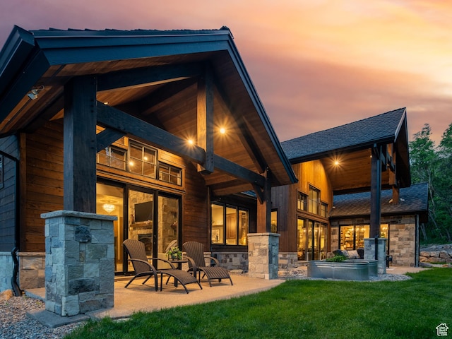 1156 N Valley View Dr, Eden, UT 84310 - back of house at dusk with a yard, stone siding, a shingled roof, and a patio