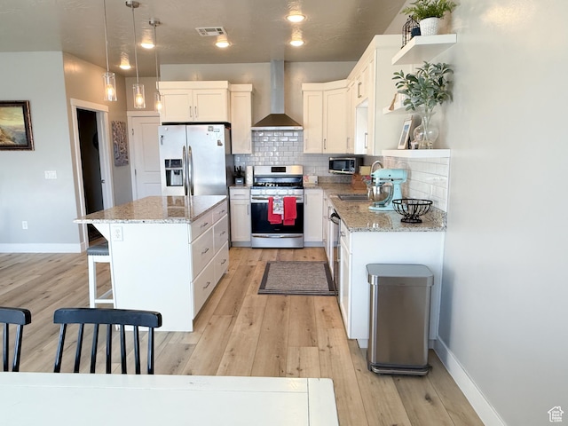 5893 S Kastra Ln, St George, UT 84790 - kitchen with stainless steel appliances, wall chimney range hood, a kitchen island, white cabinets, and light wood finished floors