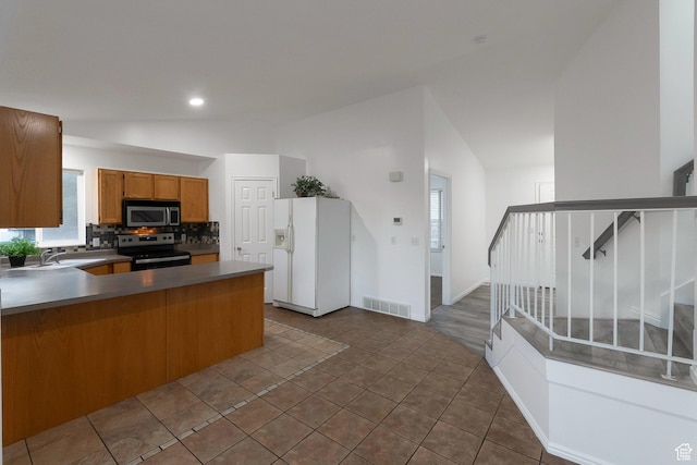 3388 W Briar Dr S, West Jordan, UT 84084 - kitchen with appliances with stainless steel finishes, vaulted ceiling, brown cabinets, a peninsula, and decorative backsplash