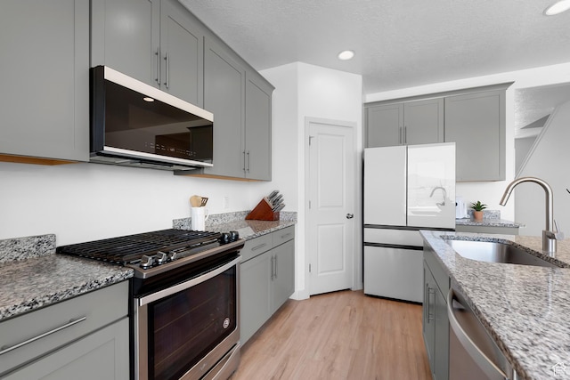 1815 E Thunder Gulch Rd, Eagle Mountain, UT 84005 - kitchen featuring appliances with stainless steel finishes, gray cabinets, a sink, light stone countertops, and light wood-style floors