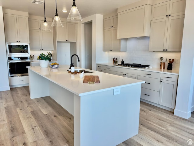 525 N 3380 W Unit 16, Hurricane, UT 84737 - kitchen with appliances with stainless steel finishes, a sink, light wood-type flooring, a kitchen island with sink, and tasteful backsplash