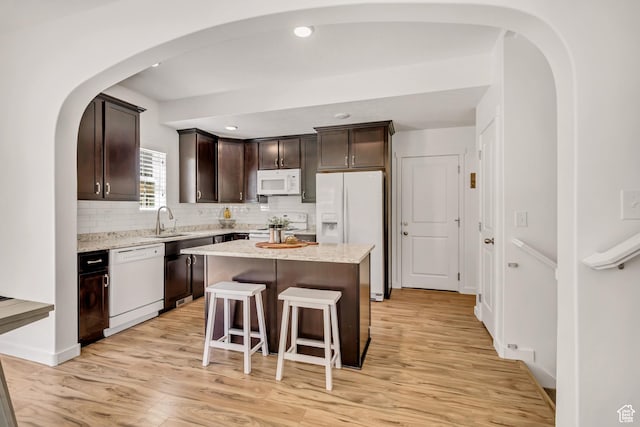 4988 W Mellow Way S, Jordan, UT 84009 - kitchen with white appliances, dark brown cabinetry, arched walkways, light wood-style flooring, and tasteful backsplash