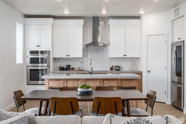 264 E Cedar Ln Unit 208, Midvale, UT 84070 - kitchen featuring wall chimney range hood, appliances with stainless steel finishes, an island with sink, white cabinetry, and decorative backsplash