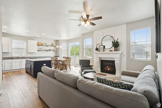693 W Fireside Ln, Stansbury Park, UT 84074 - living room with light wood-style flooring, a ceiling fan, a glass covered fireplace, and recessed lighting