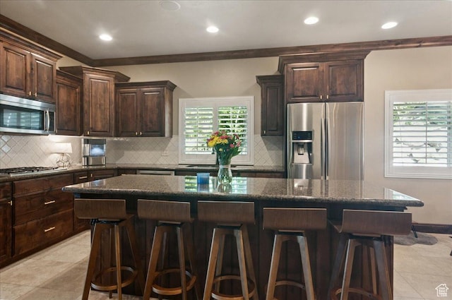 4280 S Scenic Cir E, Bountiful, UT 84010 - kitchen with appliances with stainless steel finishes, a breakfast bar area, dark brown cabinets, decorative backsplash, and dark stone countertops