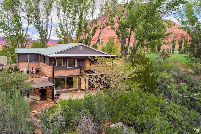 7020 E Creekside Ln, Castle Valley, UT 84532 - rear view of house with brick siding, a patio, a chimney, and metal roof