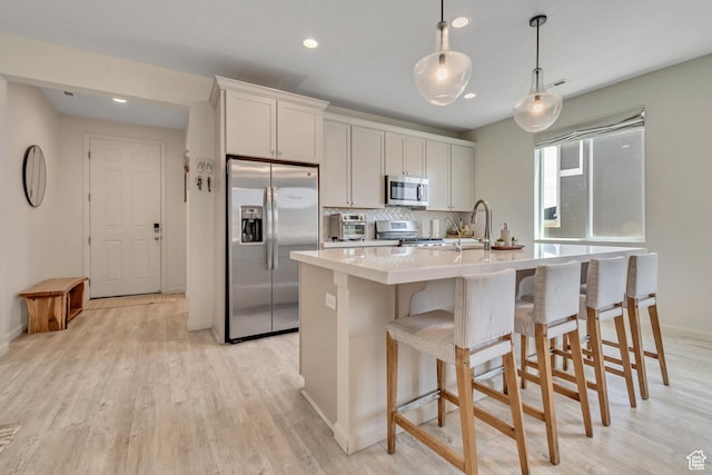 2103 N Elderberry Dr W Unit 222, Saratoga Springs, UT 84045 - kitchen with appliances with stainless steel finishes, light countertops, an island with sink, light wood-style floors, and decorative backsplash