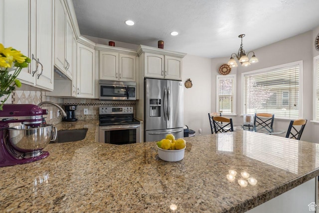 7819 S Spruce Tree Ln, Sandy, UT 84094 - kitchen with stainless steel appliances, a chandelier, decorative backsplash, a peninsula, and light stone countertops