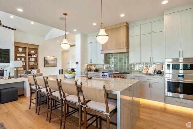 812 N 780 W, American Fork, UT 84003 - kitchen featuring appliances with stainless steel finishes, a kitchen bar, a center island with sink, backsplash, and light wood finished floors