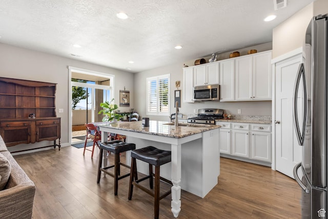 1165 W Silver Hollow Rd, Syracuse, UT 84075 - kitchen featuring appliances with stainless steel finishes, wood finished floors, white cabinetry, light stone countertops, and a breakfast bar area