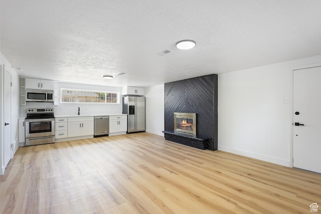 533 N 700 E, Orem, UT 84097 - unfurnished living room featuring a sink, light wood-type flooring, a textured ceiling, a fireplace, and baseboards