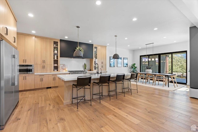 11527 S River Front Pkwy W, South Jordan, UT 84095 - kitchen featuring light brown cabinetry, appliances with stainless steel finishes, light wood-type flooring, a sink, and a large island with sink
