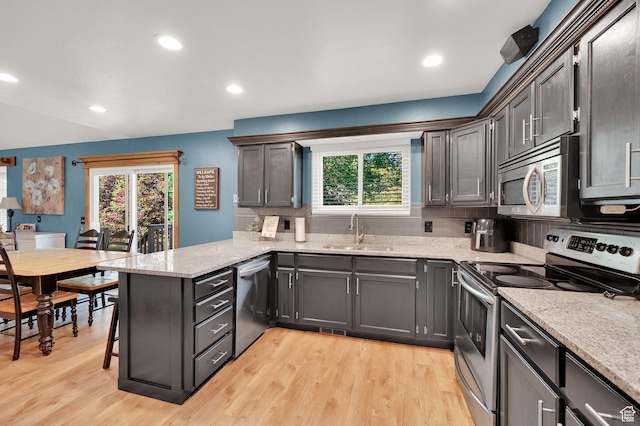 6767 S 1600 W, West Jordan, UT 84084 - kitchen featuring appliances with stainless steel finishes, a sink, a peninsula, backsplash, and light wood-style floors
