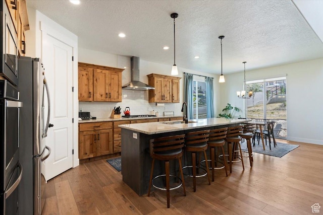 1046 W Seasons View Ct, Lehi, UT 84043 - kitchen featuring wall chimney exhaust hood, brown cabinetry, a sink, gas cooktop, and an island with sink