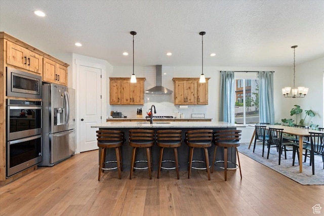 1046 W Seasons View Ct, Lehi, UT 84043 - kitchen with appliances with stainless steel finishes, wall chimney range hood, light wood-type flooring, a kitchen island with sink, and a breakfast bar area