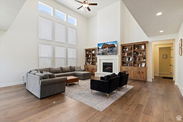 1046 W Seasons View Ct, Lehi, UT 84043 - living area with a high ceiling, a ceiling fan, light wood-style flooring, a glass covered fireplace, and baseboards