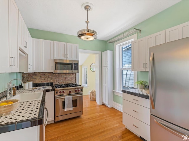 218 E Fifth Ave, Salt Lake City, UT 84103 - kitchen with appliances with stainless steel finishes, a sink, backsplash, white cabinetry, and light wood-style floors