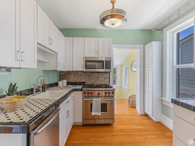 218 E Fifth Ave, Salt Lake City, UT 84103 - kitchen with appliances with stainless steel finishes, a sink, white cabinetry, light wood-type flooring, and tasteful backsplash