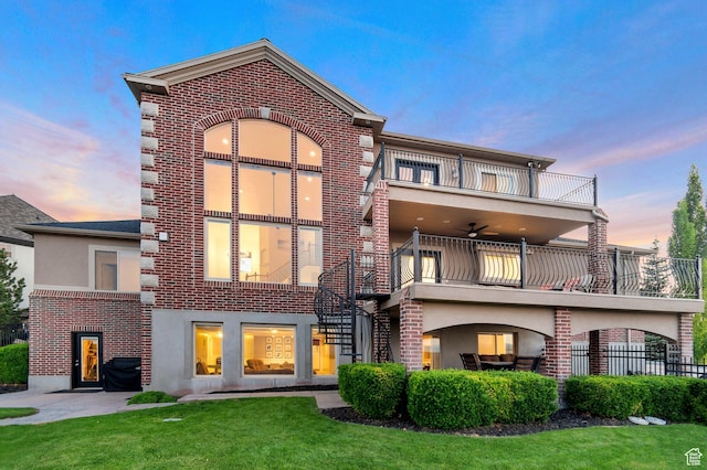 14709 S Cedar Knoll Cir, Herriman, UT 84096 - back of property at dusk featuring a balcony, brick siding, a yard, stucco siding, and stairway