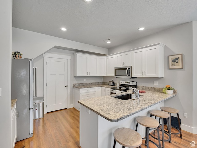 901 E 775 N, Layton, UT 84041 - kitchen featuring stainless steel appliances, a peninsula, light wood-style flooring, white cabinetry, and a kitchen bar