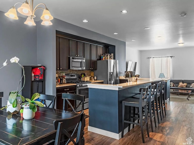 5103 W Laureston Way, Herriman, UT 84096 - kitchen with appliances with stainless steel finishes, dark brown cabinetry, dark wood-type flooring, a center island with sink, and backsplash