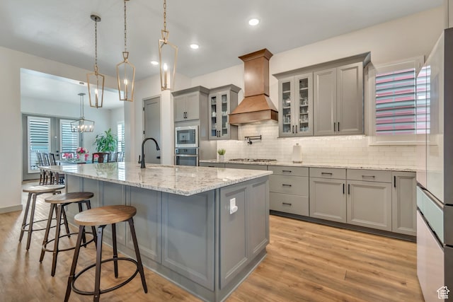 11579 S Pebble Pond Rd, South Jordan, UT 84009 - kitchen with gray cabinetry, custom exhaust hood, appliances with stainless steel finishes, a kitchen island with sink, and backsplash