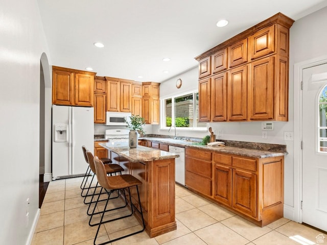 1146 E Harvard Ave S, Salt Lake City, UT 84105 - kitchen with white appliances, a center island, a kitchen bar, arched walkways, and light tile patterned floors