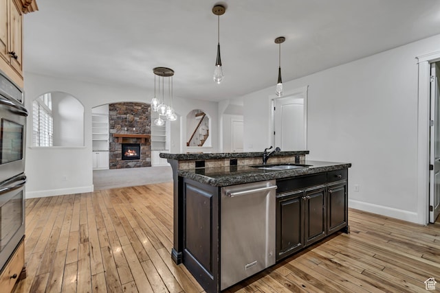 1498 W Mule Train Dr, Bluffdale, UT 84065 - kitchen featuring stainless steel appliances, a sink, a stone fireplace, light wood-style flooring, and baseboards