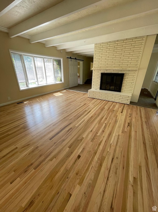 3599 E Oakview Dr, Millcreek, UT 84124 - unfurnished living room featuring a barn door, beamed ceiling, wood finished floors, and a brick fireplace
