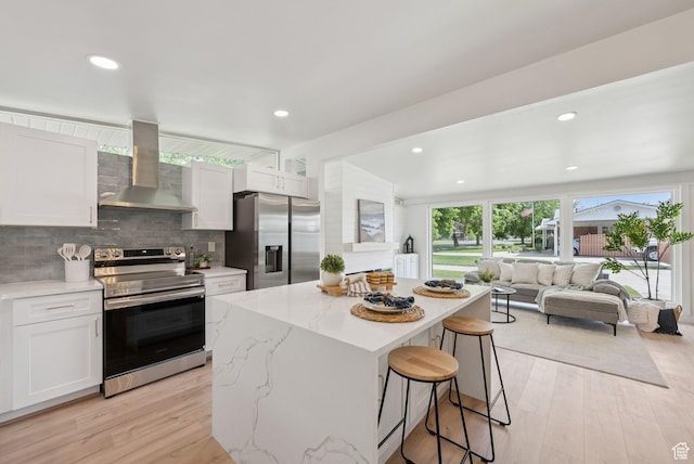 4194 S Bennion Rd, Taylorsville, UT 84129 - kitchen featuring appliances with stainless steel finishes, wall chimney range hood, a kitchen bar, a kitchen island, and white cabinets