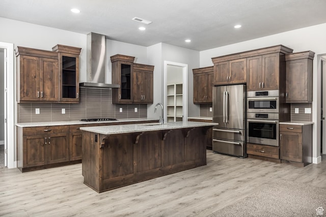 1861 N Mountain View Dr, Washington, UT 84780 - kitchen with appliances with stainless steel finishes, wall chimney range hood, decorative backsplash, a kitchen breakfast bar, and light wood-type flooring