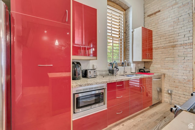 342 W 200 S Unit 107, Salt Lake City, UT 84101 - kitchen with light wood-style flooring, brick wall, appliances with stainless steel finishes, red cabinets, and a sink